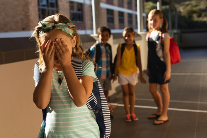 Front view of school friends bullying a crying girl in hallway of elementary school